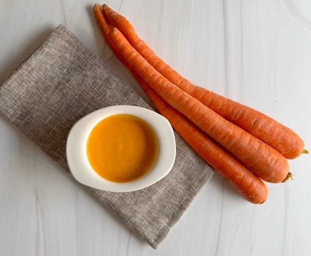 Napkin with white ramakin filled with creamy orange ginger miso salad dressing and 3 carrots on the side.